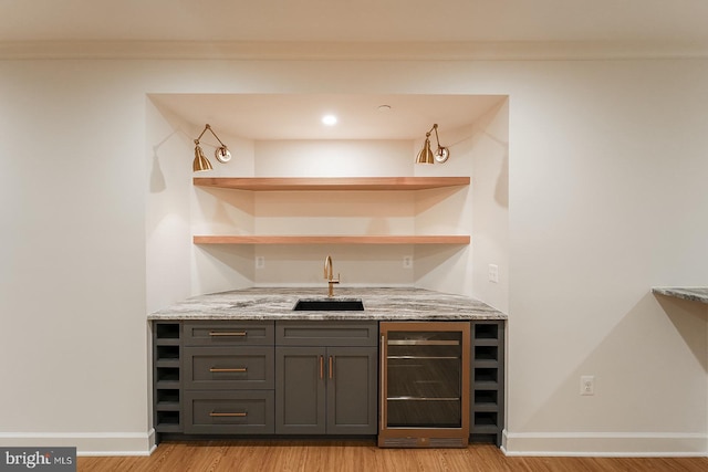 bar with light stone counters, wine cooler, light wood-type flooring, and sink