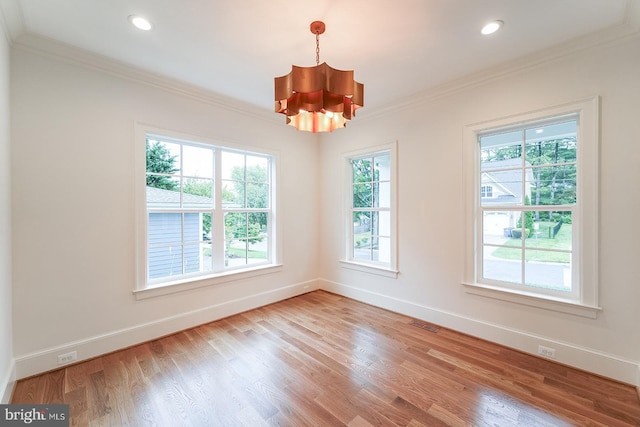 spare room featuring ornamental molding, light wood-type flooring, a chandelier, and a healthy amount of sunlight