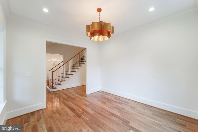 empty room with a notable chandelier, ornamental molding, and hardwood / wood-style flooring