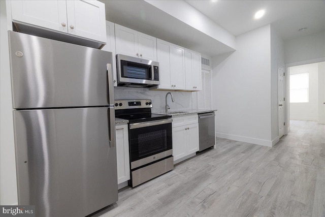 kitchen featuring light stone counters, light hardwood / wood-style floors, tasteful backsplash, white cabinetry, and stainless steel appliances