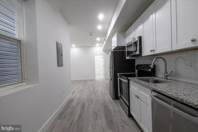 kitchen with stainless steel appliances, white cabinets, light hardwood / wood-style floors, and stone counters