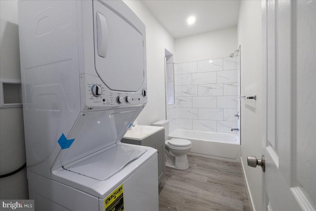 full bathroom with tiled shower / bath, vanity, wood-type flooring, stacked washer / dryer, and toilet