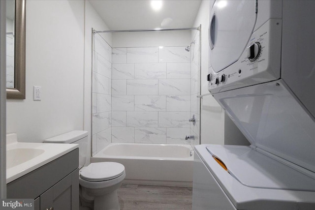 full bathroom featuring wood-type flooring, stacked washing maching and dryer, tiled shower / bath combo, vanity, and toilet