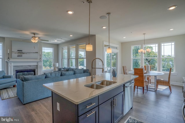 kitchen featuring an island with sink, hanging light fixtures, light stone countertops, and sink