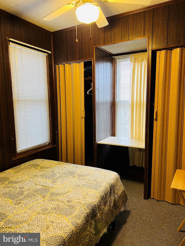 carpeted bedroom featuring ceiling fan and wooden walls