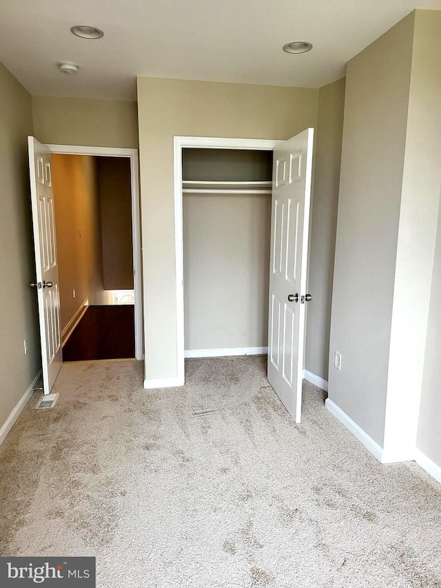 unfurnished bedroom with light colored carpet and a closet