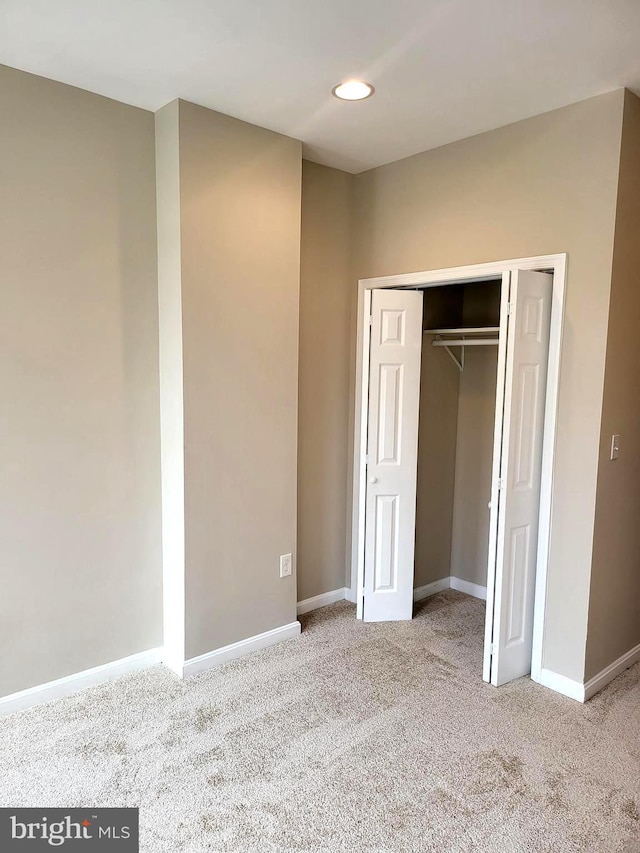 unfurnished bedroom with light colored carpet and a closet