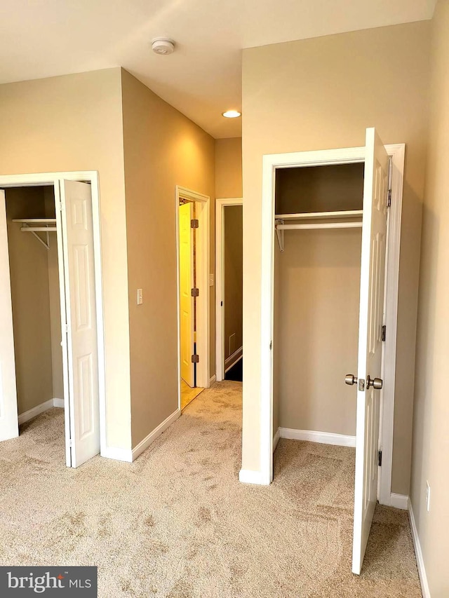 unfurnished bedroom featuring light colored carpet and two closets