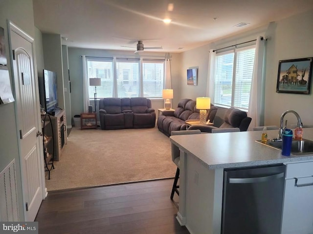 kitchen with ceiling fan, stainless steel dishwasher, a breakfast bar, sink, and dark hardwood / wood-style flooring