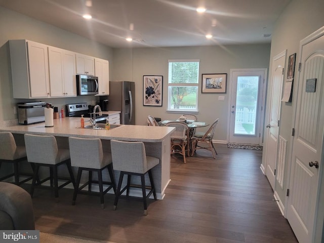 kitchen with sink, white cabinetry, stainless steel appliances, a kitchen bar, and dark hardwood / wood-style flooring