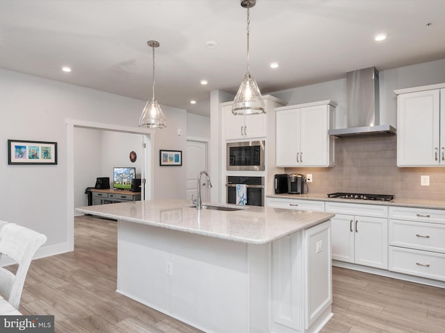 kitchen with a kitchen island with sink, white cabinetry, light hardwood / wood-style floors, and wall chimney range hood