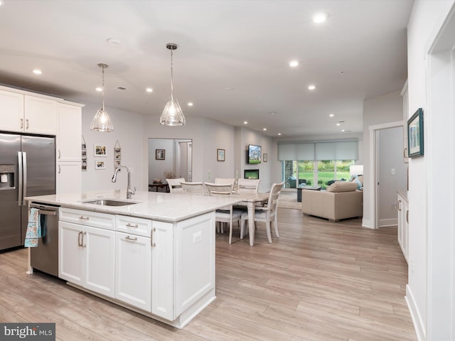 kitchen with white cabinetry, pendant lighting, stainless steel appliances, a center island with sink, and sink