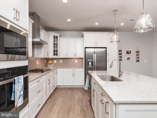 kitchen with white cabinets, stainless steel appliances, light hardwood / wood-style flooring, sink, and wall chimney range hood