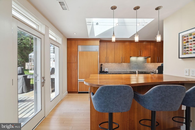 kitchen with hanging light fixtures, tasteful backsplash, a breakfast bar area, light hardwood / wood-style flooring, and paneled refrigerator