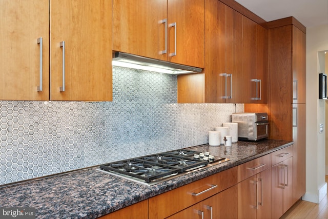 kitchen with dark stone countertops, backsplash, light hardwood / wood-style floors, and stainless steel gas cooktop