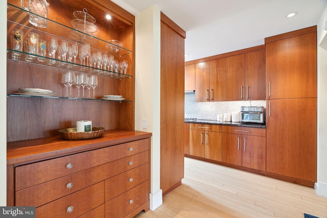 bar with dark stone counters, decorative backsplash, and light hardwood / wood-style flooring