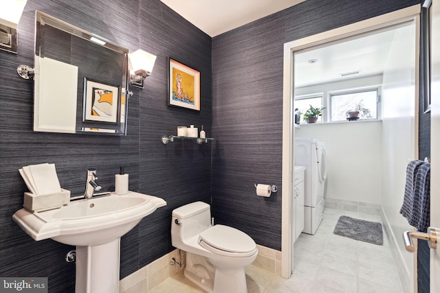 bathroom with tile walls, tile patterned flooring, toilet, and washer and dryer