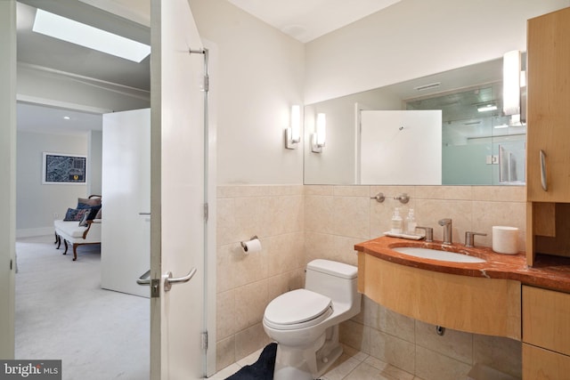 bathroom featuring a skylight, vanity, tile walls, and toilet