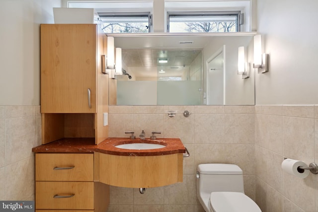 bathroom featuring tile walls, toilet, walk in shower, and sink