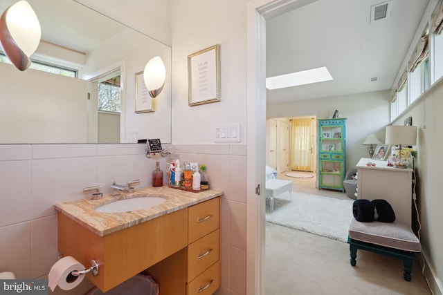 bathroom with tile walls, a skylight, vanity, and toilet