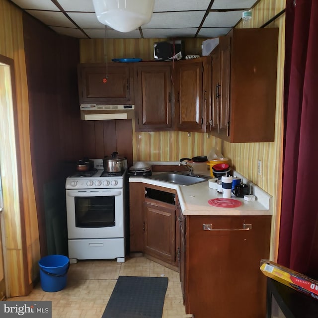 kitchen with gas range gas stove, wood walls, a drop ceiling, sink, and extractor fan