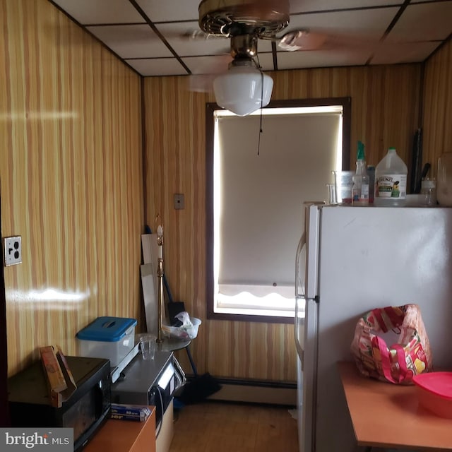 kitchen with a paneled ceiling, wooden walls, baseboard heating, and white refrigerator