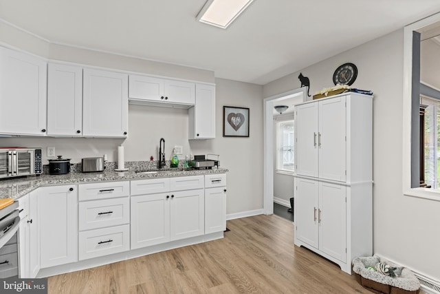 kitchen with light hardwood / wood-style flooring, white cabinets, light stone counters, and sink