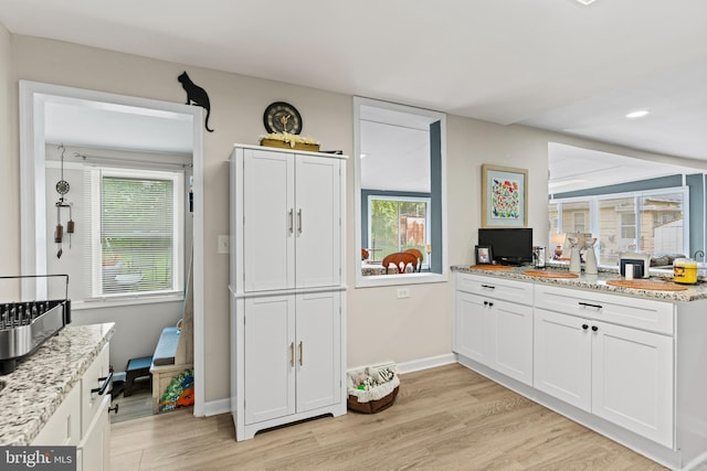 kitchen featuring light wood-type flooring, white cabinetry, light stone counters, and a wealth of natural light