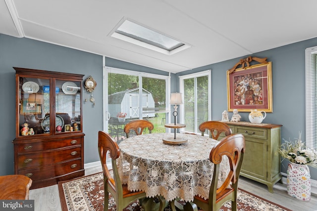 dining area with vaulted ceiling with skylight and light wood-type flooring