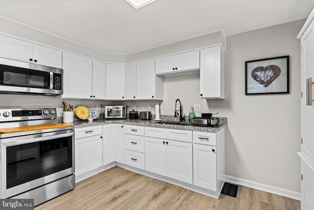 kitchen with sink, white cabinetry, appliances with stainless steel finishes, dark stone countertops, and light hardwood / wood-style floors