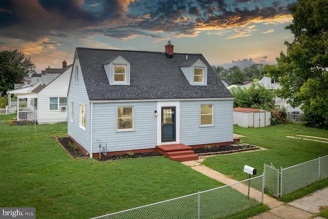 cape cod home featuring a lawn and a storage unit