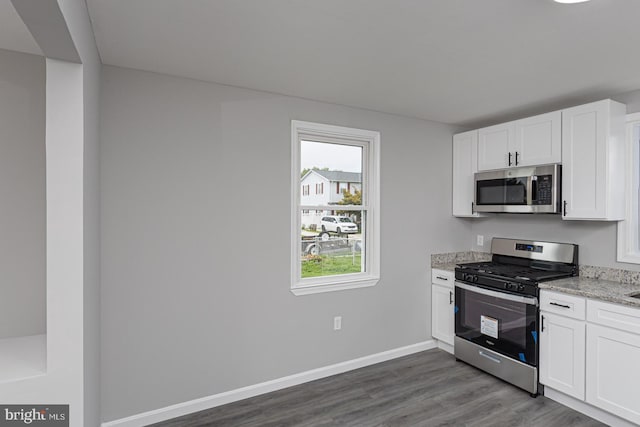 kitchen with appliances with stainless steel finishes, hardwood / wood-style flooring, light stone countertops, and white cabinets