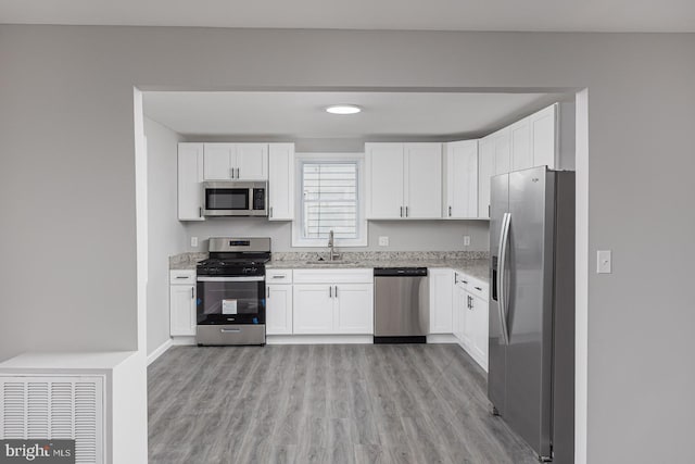 kitchen with stainless steel appliances, sink, white cabinetry, and light hardwood / wood-style flooring