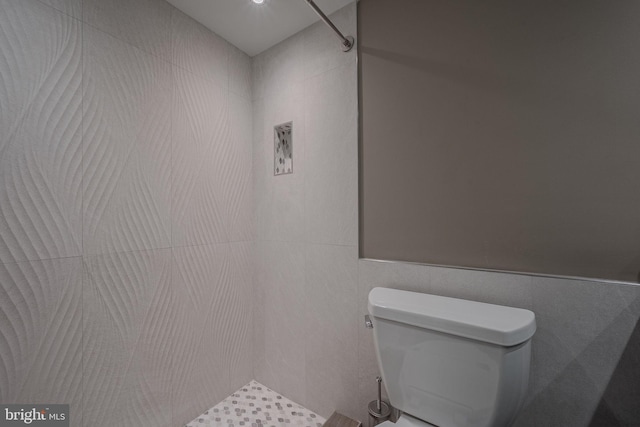 bathroom with tile walls, a tile shower, and toilet