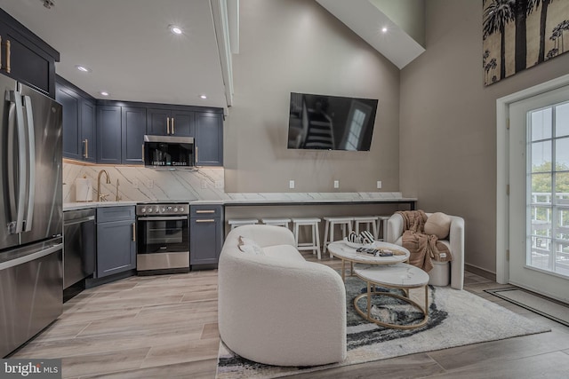 kitchen with sink, light hardwood / wood-style flooring, stainless steel appliances, backsplash, and high vaulted ceiling