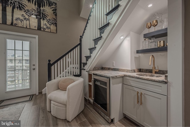 bar with light stone counters, beverage cooler, light hardwood / wood-style floors, and white cabinetry