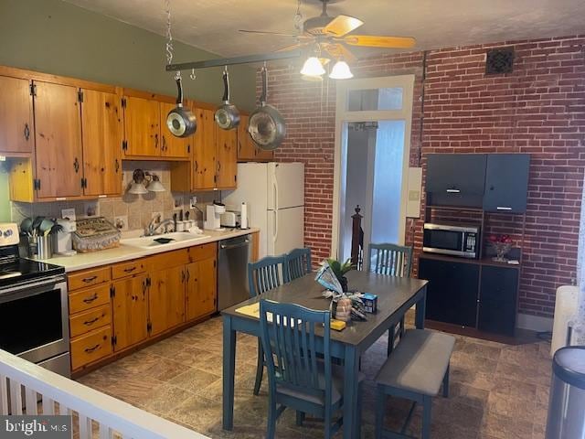 kitchen with tasteful backsplash, appliances with stainless steel finishes, sink, ceiling fan, and brick wall