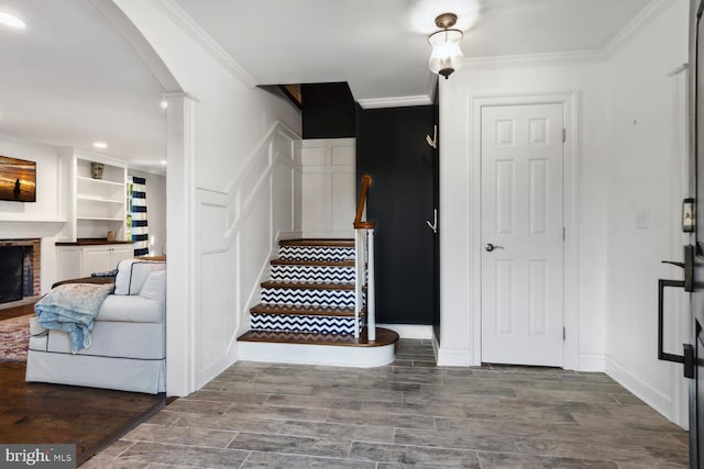 stairs with hardwood / wood-style floors, crown molding, and a fireplace