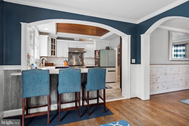 kitchen featuring appliances with stainless steel finishes, a kitchen bar, white cabinetry, light hardwood / wood-style floors, and ornamental molding