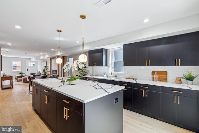 kitchen featuring hanging light fixtures, decorative backsplash, a kitchen island, light wood-type flooring, and sink