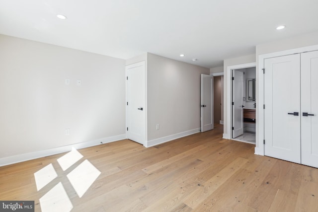 unfurnished bedroom featuring a closet, ensuite bath, and light hardwood / wood-style floors