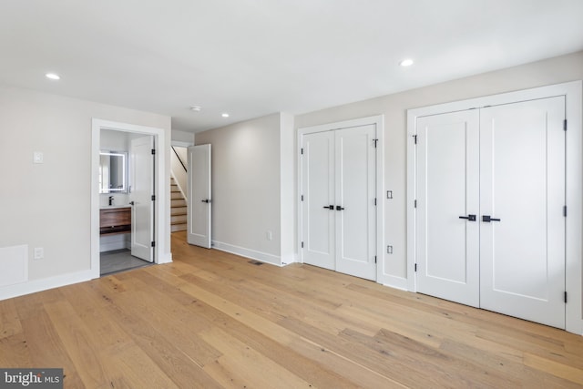 unfurnished bedroom with connected bathroom, multiple closets, and light wood-type flooring