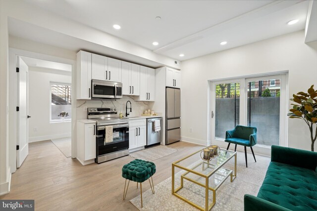 kitchen with tasteful backsplash, white cabinets, stainless steel appliances, light hardwood / wood-style flooring, and sink