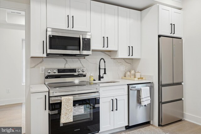 kitchen featuring white cabinets, light wood-type flooring, appliances with stainless steel finishes, and backsplash