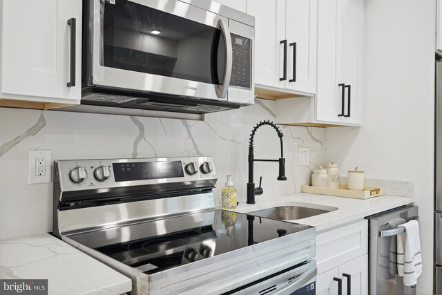 kitchen featuring decorative backsplash, stainless steel appliances, white cabinetry, and light stone countertops