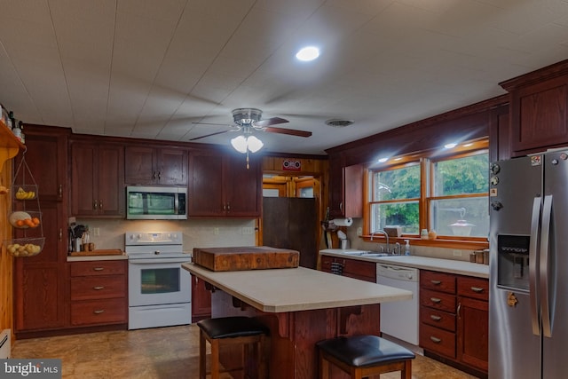 kitchen featuring ceiling fan, sink, appliances with stainless steel finishes, a center island, and a breakfast bar area