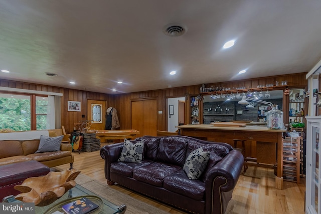 living room featuring wooden walls, light hardwood / wood-style flooring, and indoor bar