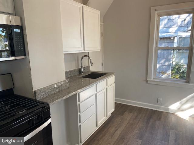 kitchen with dark hardwood / wood-style floors, black range with gas cooktop, sink, light stone countertops, and white cabinets