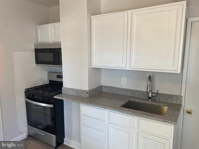 kitchen with light stone countertops, sink, stainless steel gas range oven, and white cabinets