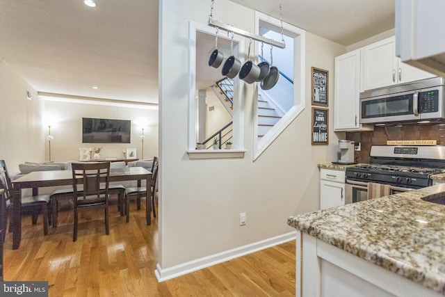 kitchen featuring light stone countertops, appliances with stainless steel finishes, light hardwood / wood-style floors, and white cabinetry